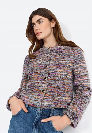 Giacca multicolore con texture in tonalità di viola, arancione e grigio, dotata di colletto, bottoni e maniche lunghe, abbinata a jeans di denim.