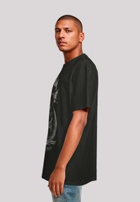 Black cotton t-shirt with a loose fit, round neckline, and short sleeves. Features a prominent graphic design on the front.