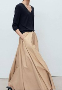 Granatowy sweter z dekoltem w serek i długimi rękawami w połączeniu z zwiewną, beżową spódnicą sięgającą kostek, wyposażoną w elastyczny pas i kieszenie.