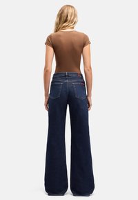 Dżinsy o szerokich nogawkach w ciemnoniebieskim kolorze, z wysokim stanem, wykonane z denimu. Posiadają kieszenie i subtelny tylny detal z logo. Brązowa dopasowana bluzka z krótkimi rękawami.