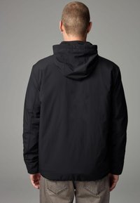 Sort hættetrøje med en glat tekstur, der har en løs pasform og elastiske manchetter. Synlige sømme og et minimalistisk design.