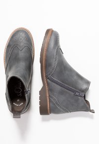 Šedé kožené kotníkové boty s dekorativním brogue zdobením, bočním zipem, robustní hnědou podrážkou a texturovaným povrchem.