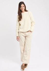 Maglione beige trapuntato con colletto rotondo, abbinato a pantaloni baggy beige chiaro. Le scarpe con stampa leopardata marrone completano il look.