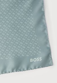 Γωνία υφάσματος ανοιχτού μπλε με σχέδιο, ραμμένες άκρες και λευκό λογότυπο "BOSS" τυπωμένο κοντά στην άκρη σε λευκό φόντο.