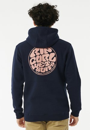 Granatowy hoodie z dużą różową okrągłą grafiką z tyłu, na której widnieje napis "RIP CURL WETSUITS" w pogrubionej, zaokrąglonej czcionce. Miękka tkanina, luźny krój.