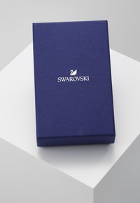 Caixa de presente texturizada em roxo com o logótipo branco da Swarovski na tampa, apresentando um design minimalista e formato retangular.