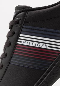 Zwarte synthetische sneakers met een gestructureerde afwerking, voorzien van een gestreept ontwerp in marineblauw, rood en wit, met het "HILFIGER"-logo.
