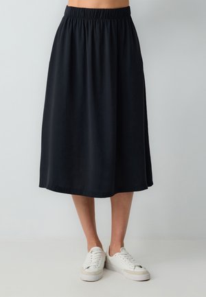 Jupe midi noire avec une taille élastique, au design fluide et texture douce, associée à des baskets blanches.