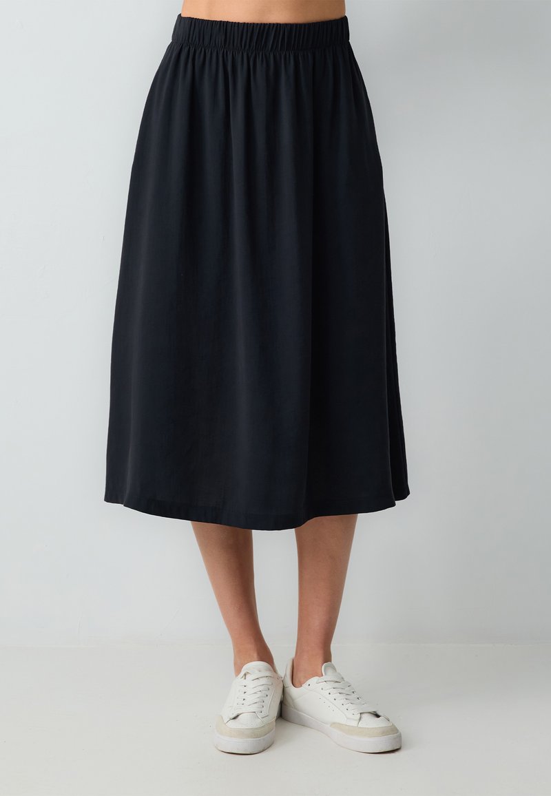 Jupe midi noire avec une taille élastique, au design fluide et texture douce, associée à des baskets blanches.