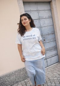 T-shirt tie-dye bleu clair avec le texte "en besoin de vitamine mer", associé à une jupe midi en denim. Style décontracté, coupe ample, avec des manches courtes.