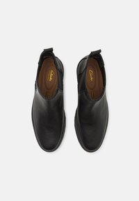 Zapatos negros de cuero sin cordones con una textura suave, puntera redondeada y un detalle de costura sutil. El interior cuenta con una plantilla acolchada.