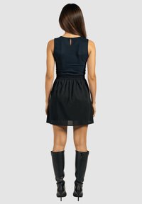 Vestido sin mangas de color marino con un cuerpo ajustado, cintura elástica y falda fluida, combinado con botas negras hasta la rodilla. Detalle de abertura en la parte posterior.