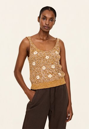 Gelber Strick-Tanktop mit weißer floralem Stickerei, präsentiert mit einem Rundhalsausschnitt und geripptem Saum; kombiniert mit lockeren, dunklen Hosen.