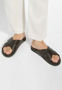 Brown leather slide sandals featuring a crossed strap design. Smooth texture and flat sole, suitable for casual wear.