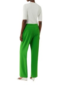 Zielone spodnie o szerokich nogawkach wykonane z gładkiego materiału, z wysokim stanem i tylnymi kieszeniami. Zestawione z dopasowanym białym topem i jasnym obuwiem.