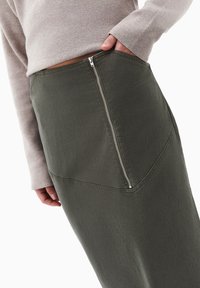 Oliven grøn nederdel med struktureret stof, med en synlig sidelukning og skrå sømme. Sammen med en lys grå langærmet bluse.