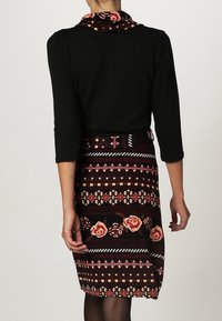 Top nero con maniche lunghe e collo a sacco, abbinato a una gonna fino al ginocchio con motivi floreali e geometrici in bordeaux e crema.