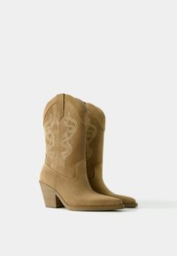 Brązowe kowbojki zamszowe z zakończeniem w szpic, 3-calowym słupkowym obcasem i haftowanym wzorem spiralnym na cholewce.