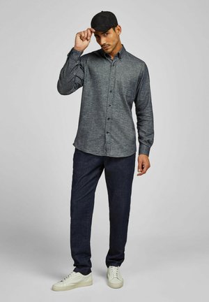 Dark blue, long-sleeve button-up shirt with a textured fabric. Paired with dark blue pants and white sneakers. Wearing a black cap.