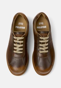 Zapatillas de cuero marrón con cordones beige, puntera redondeada y sutiles detalles de costura. La plantilla presenta la marca "CAMPER" y "PELOTAS".