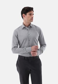 Kariertes Hemd mit Kragen in Schwarz-Weiß im Gingham-Muster mit langen Ärmeln, kombiniert mit dunklen Hosen. Baumwollmischgewebe, glatte Textur.