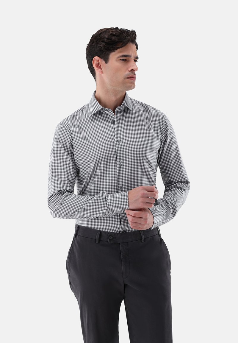 Kariertes Hemd mit Kragen in Schwarz-Weiß im Gingham-Muster mit langen Ärmeln, kombiniert mit dunklen Hosen. Baumwollmischgewebe, glatte Textur.