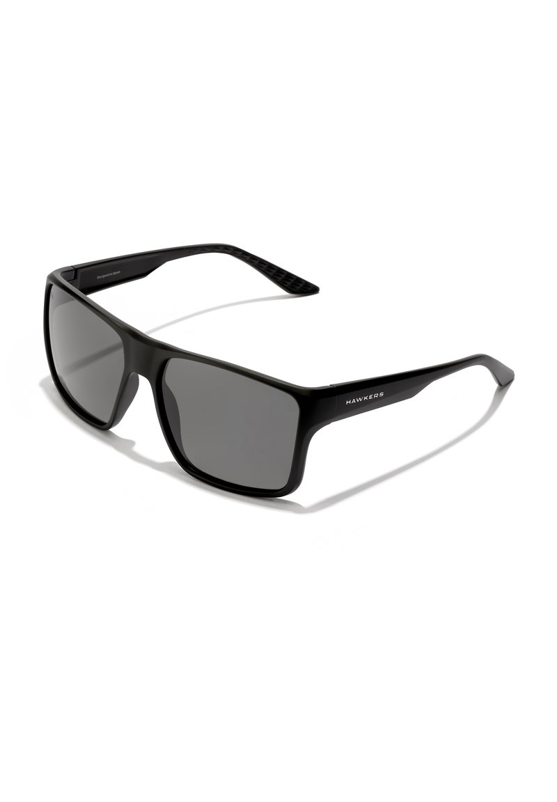 Ochelari de soare negri cu lentile dreptunghiulare, finisaj mat și brațe texturate; prezintă un logo pe lateral și un design robust, unghiular.
