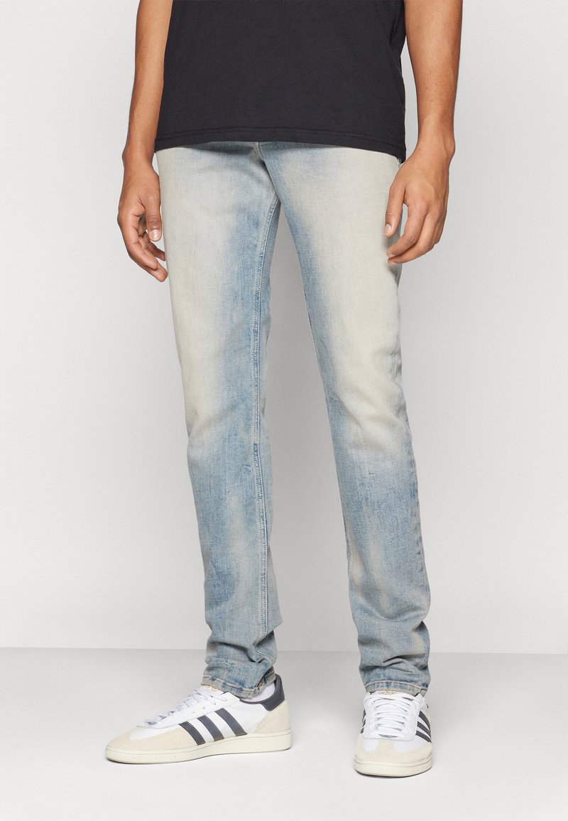 Lichtblauwe denim jeans met een vervaagd uiterlijk, tapered fit en subtiele whiskers. Gekozen in combinatie met witte en grijze sneakers.