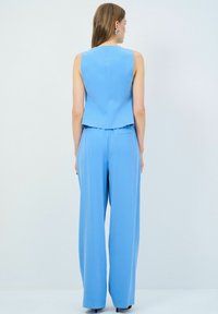 Niebieski dwuczęściowy zestaw składający się z bezrękawnikowej bluzki i spodni z szerokimi nogawkami, wykonany z gładkiego materiału o prostym designie i minimalnych szwach.