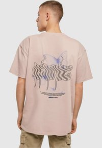 Pink cotton t-shirt with a loose fit, featuring a graphic design of a butterfly and stylized text on the back. Short sleeves, round neck.
