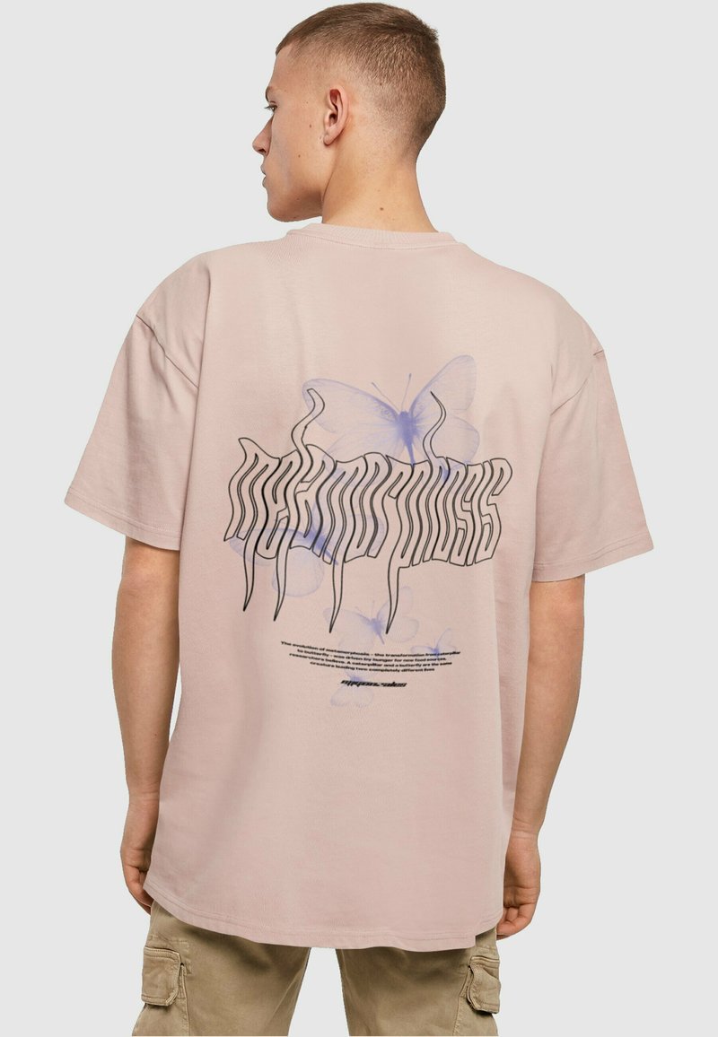 Pink cotton t-shirt with a loose fit, featuring a graphic design of a butterfly and stylized text on the back. Short sleeves, round neck.