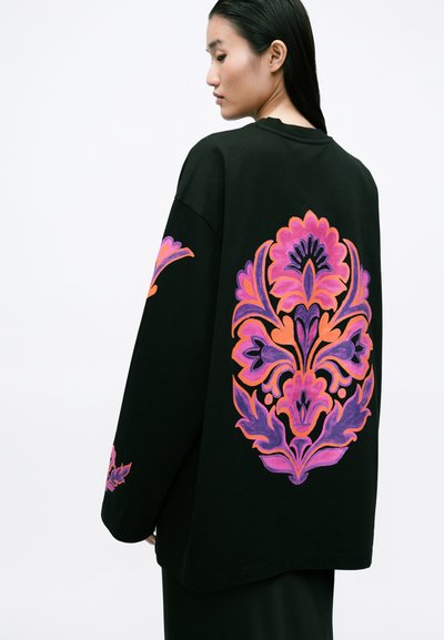 Čierny oversized sveter s živými kvetinovými vzormi v ružovej, fialovej a oranžovej farbe na chrbte a na jednom rukáve. Mäkká tkanina, voľný strih.