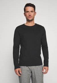 Tricou negru cu mânecă lungă, material neted, guler rotund, design ajustat, asociat cu pantaloni gri deschis cu carouri, stil minimalistic.
