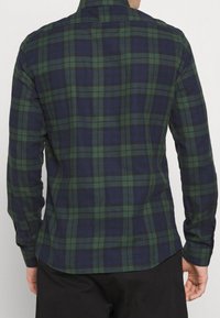 Camisa de cuadros de manga larga en verde oscuro y azul marino con patrón de cuadros. Presenta un cuello y puños abotonados, hecha de tela tejida.