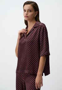 Korte mouwen blouse in donkerrood met een ruitpatroon in lichtere tinten. Gemaakt van een soepel materiaal met een relaxte pasvorm en kraag.