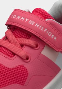 Ροζ αθλητικό παπούτσι με υλικά από δίχτυ και συνθετικά. Διαθέτει λουράκι με την επωνυμία "TOMMY HILFIGER", υφασμένα κορδόνια και ροζ λεπτομέρειες.