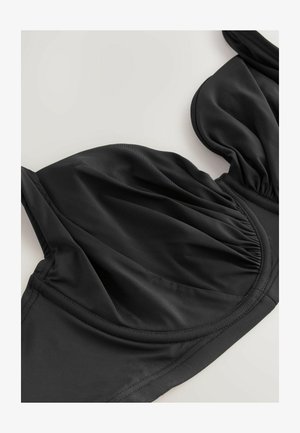 Svart bikiniöverdel med samlad textur, mjukt material, underwire-stöd och justerbara axelband. Slät yta med sömlösa kanter.