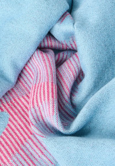 Tissu tricoté doux avec des sections bleu clair et des motifs rayés diagonaux roses et blancs, présenté en gros plan sur des plis.