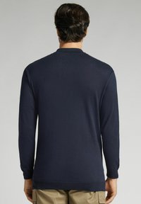 Granatowy sweter z długim rękawem i okrągłym dekoltem, z prążkowanymi mankietami i dołem. Gładka tekstura, luźny krój i minimalne detale przeszycia.