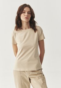 Beige aansluitend T-shirt met korte mouwen en een ronde halslijn, gemaakt van een zachte stof, gecombineerd met beige broeken. Eenvoudig, strak ontwerp.