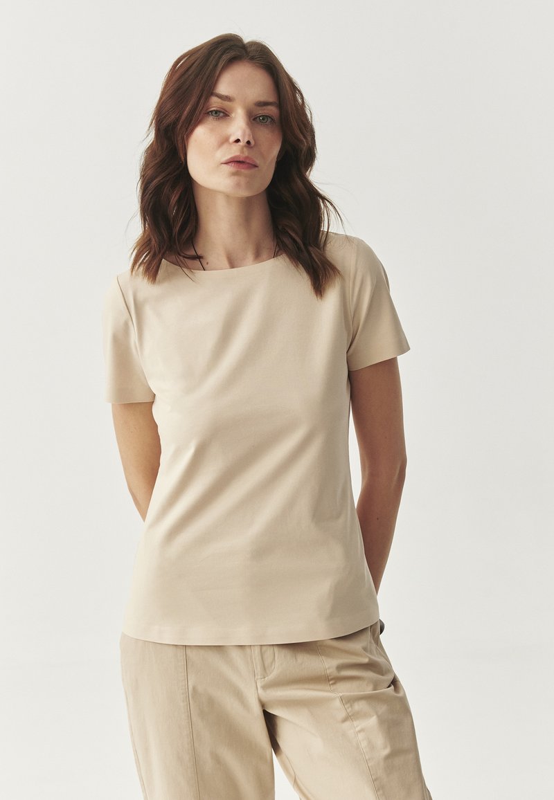 Beige aansluitend T-shirt met korte mouwen en een ronde halslijn, gemaakt van een zachte stof, gecombineerd met beige broeken. Eenvoudig, strak ontwerp.