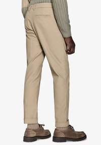 Beige, slim-fit bukser med glat stof, baglommer og opsmøg over brune sko med textureret overflade.