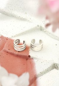 Silverring med utskurna geometriska mönster, med en slät, polerad yta. Bakgrunden visar en texturerad, flerfärgad yta.