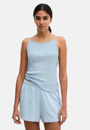 Donna che indossa una canotta a coste azzurro chiaro senza maniche e pantaloncini con vita elastica abbinati, su sfondo neutro.