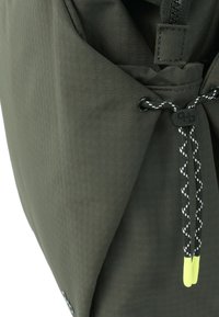 Gros plan d'un tissu vert foncé avec une fermeture éclair et un cordon noir et blanc avec des embouts en plastique jaunes et un verrou noir.