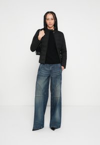 Must tikitud jope, pikkade varrukatega must särk ja laia säärega sinised teksad, millel on tikanddetailid; stiilitud mustade kontsade ja käekotiga.