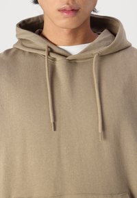 Khaki-huvtröja med snörning, med en mjuk textur och enkelt mönster, uppvisad mot en neutral bakgrund.