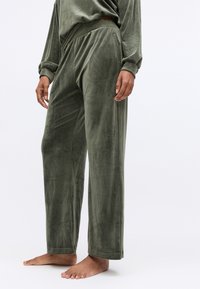 Olijfgroene velours loungebroek met een ontspannen pasvorm, voorzien van een platte tailleband en omgeslagen hems. Zachte textuur zichtbaar over de stof.