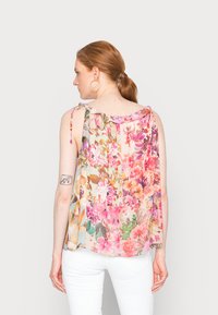 Top sem mangas floral com decote ondulado, apresentando uma mistura de flores rosas, roxas e amarelas sobre um fundo claro. Tecido suave e fluido.