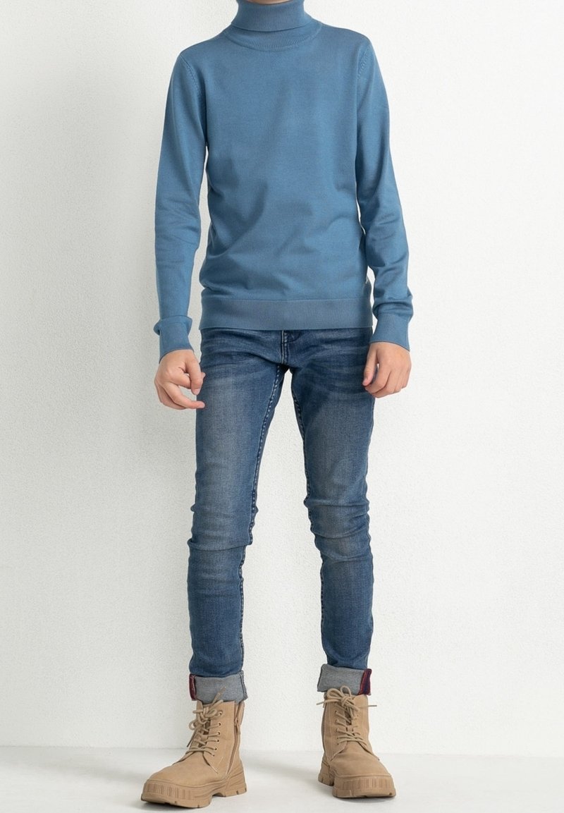 Pull à col roulé bleu, design ajusté, avec des poignets et un ourlet côtelés. Associé à un jean en denim slim fit et des bottes en cuir beige à lacets avec des semelles robustes.